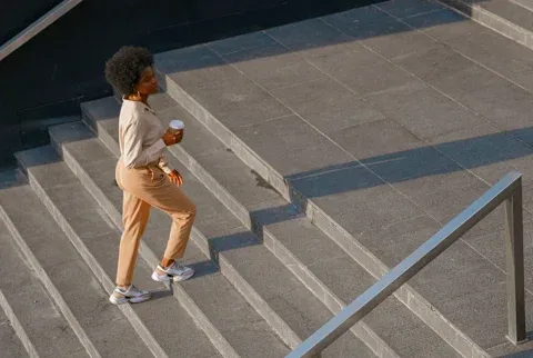 woman walks up stairs outside holding a coffee