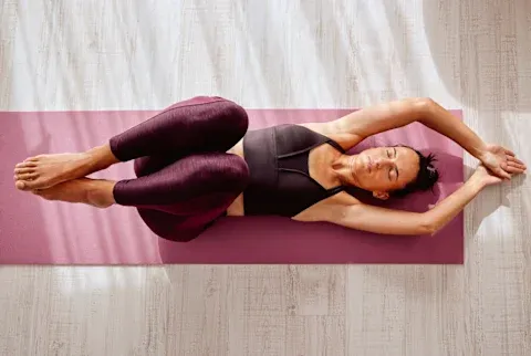 Overhead of female stretching body lying down while doing yoga on pink mat at home