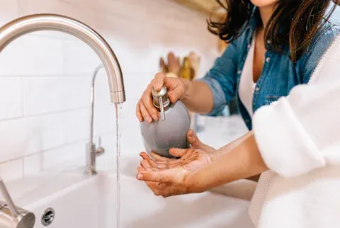 Unrecognizable woman pouring soft soap on hands of child near sink in kitchen
