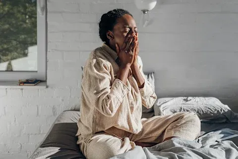 Yawning woman sitting up in bed with sun coming in through the window