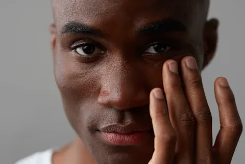 Close up of a black man with piercing eyes touching his face