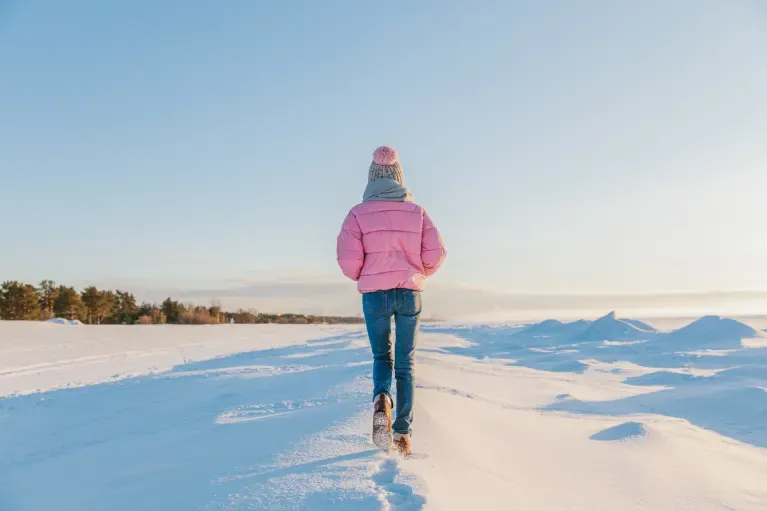 Woman in warm colorful clothes walking in the snow on a frosty sunny day
