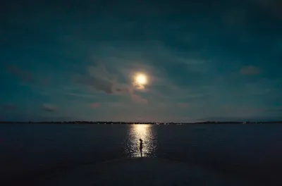 Young female silhouete at the shore with the reflected light of the moon on the sea