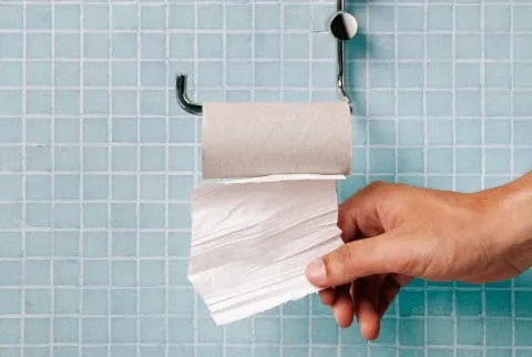 Hand pulling last square of toilet paper from the roll Hand pulling last square of toilet paper from the roll