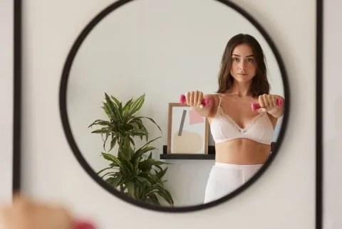 Woman lifting hand weights at home looking at herself in the mirror Woman lifting hand weights at home looking at herself in the mirror